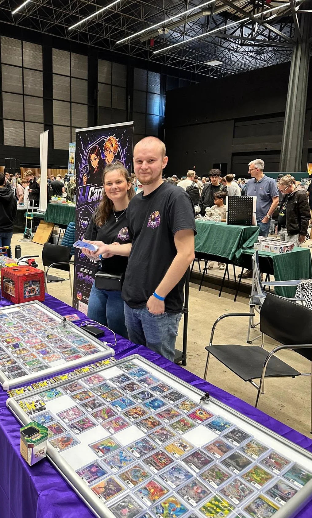 Het team van IJCardsTCG achter de stand op een kaartenbeurs, met vitrines vol Pokémon-kaarten
